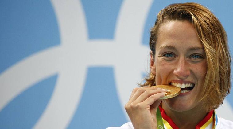 Catalan swimmer Mireia Belmonte biting her gold medal in 200m butterfly at Rio Olympics (by David Gray / Reuters)