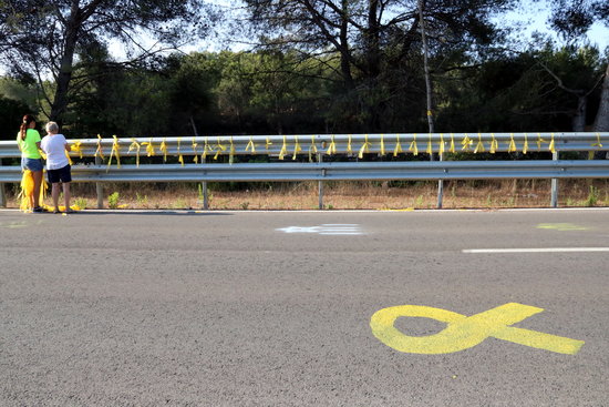 Two people placing yellow signs on a road leading to a prison where a political leader is incarcerated (by Núria Torres)
