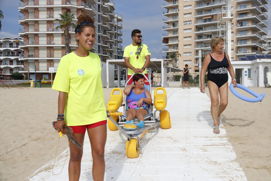 Two lifeguards help Laura Gonzàlez into the water at Torre Valentina beach (ACN)