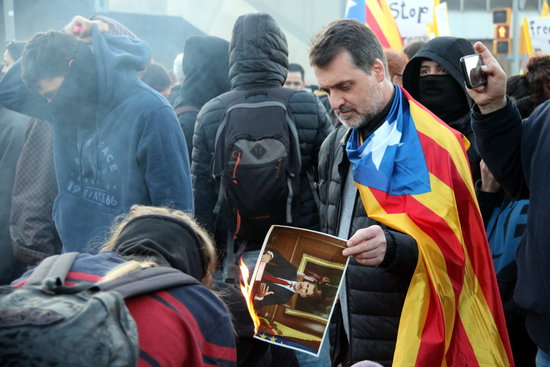 A protester wearing a Catalan independence flag burns a picture of Spain's king, Felipe VI (by Àlex Recolons)