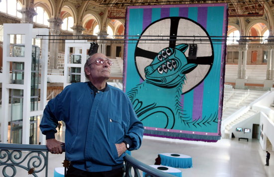 Antoni Miralda standing on a balcony in front of his 'Lamb of the Apocalypse' tapestry in the MNAC (Photo: Pau Cortina)