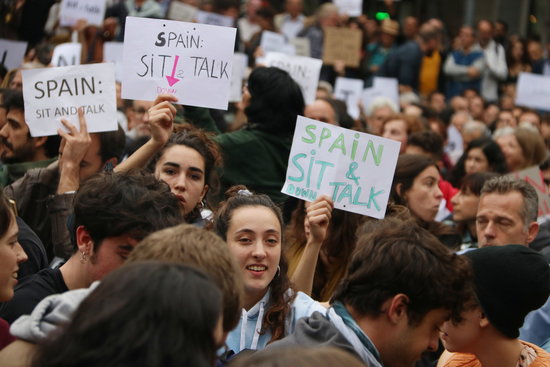 Protesters holding signs calling on Spain to 'Sit and talk' about the Catalan independence issue (by Pau Cortina)