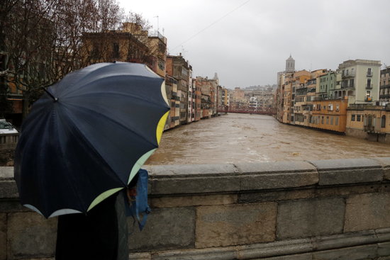 A man holding an umbrella stops to take a picture of the elevated water in the river Onyar in Girona (by Marina López)