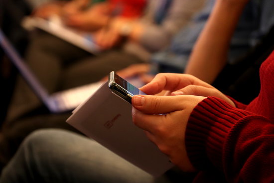 A person holding their phone during a conference (by Mar Vila)