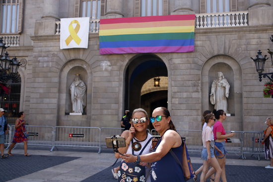 Two people take a selfie with an LGBTQI flag hanging from the Barcelona City Council building (by Sílvia Jardí)