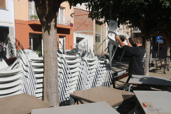 A bar owner in northern Catalonia stacks chairs and gathers terrace tables together when Covid-19 restrictions were implemented preventing bars from opening on October 16, 2020 (by Xavier Pi)
