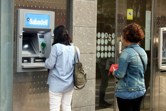 People queue to withdraw money from a Banc Sabadell ATM (by Xavier Pi)