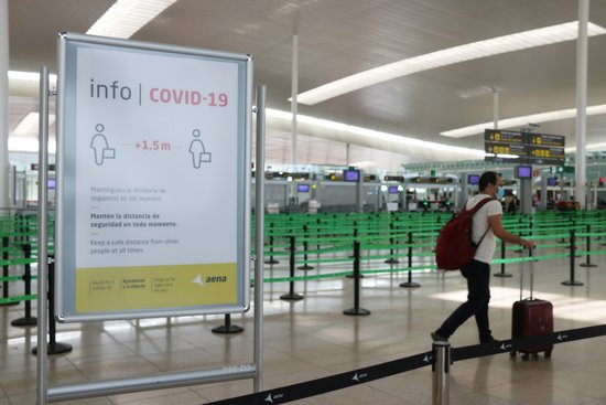 Traveller walks past a Covid-19 sign in the Barcelona airport (by Norma Vidal)