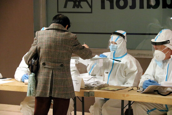 A woman votes in Barcelona in front of poll workers in hazmat suits, on February 14, 2021 (photo by Miquel Codolar)