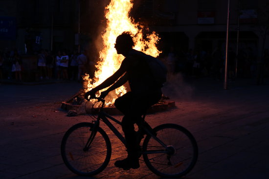 A person cycles in front of a Sant Joan bonfire in Barcelona's Plaça de la Virreina, June 23, 2019 (by Elisenda Rosanas)