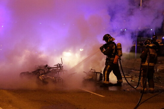 A bicycle burnt in Bogatell beach, Barcelonaand the firefighters working on putting the fire out, on September 25, 2021 (by Jordi Pujolar)