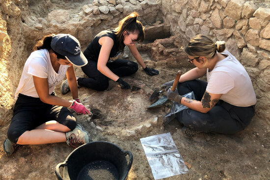 Archaeologists excavate a fireplace, with the structure of a Greek kitchen from the 6th century BC behind, Empúries (MAC-Empúries)