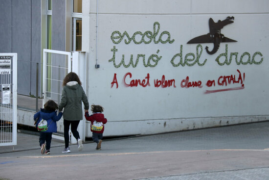 A mother with her children entering the Turó del Drac school, in Canet de Mar, where a graffiti reads 'We want classes in Catalan in Canet', on December 9, 2021 (by Jordi Pujolar)