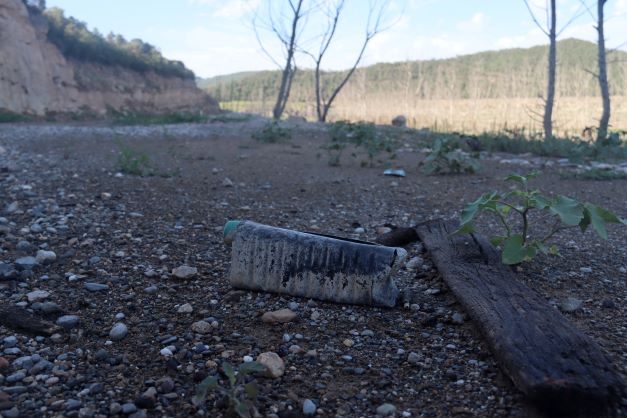 Closeup image of the dry ground and a weathered plastic bottle in the Rialb reservoir (by Albert Lijarcio)