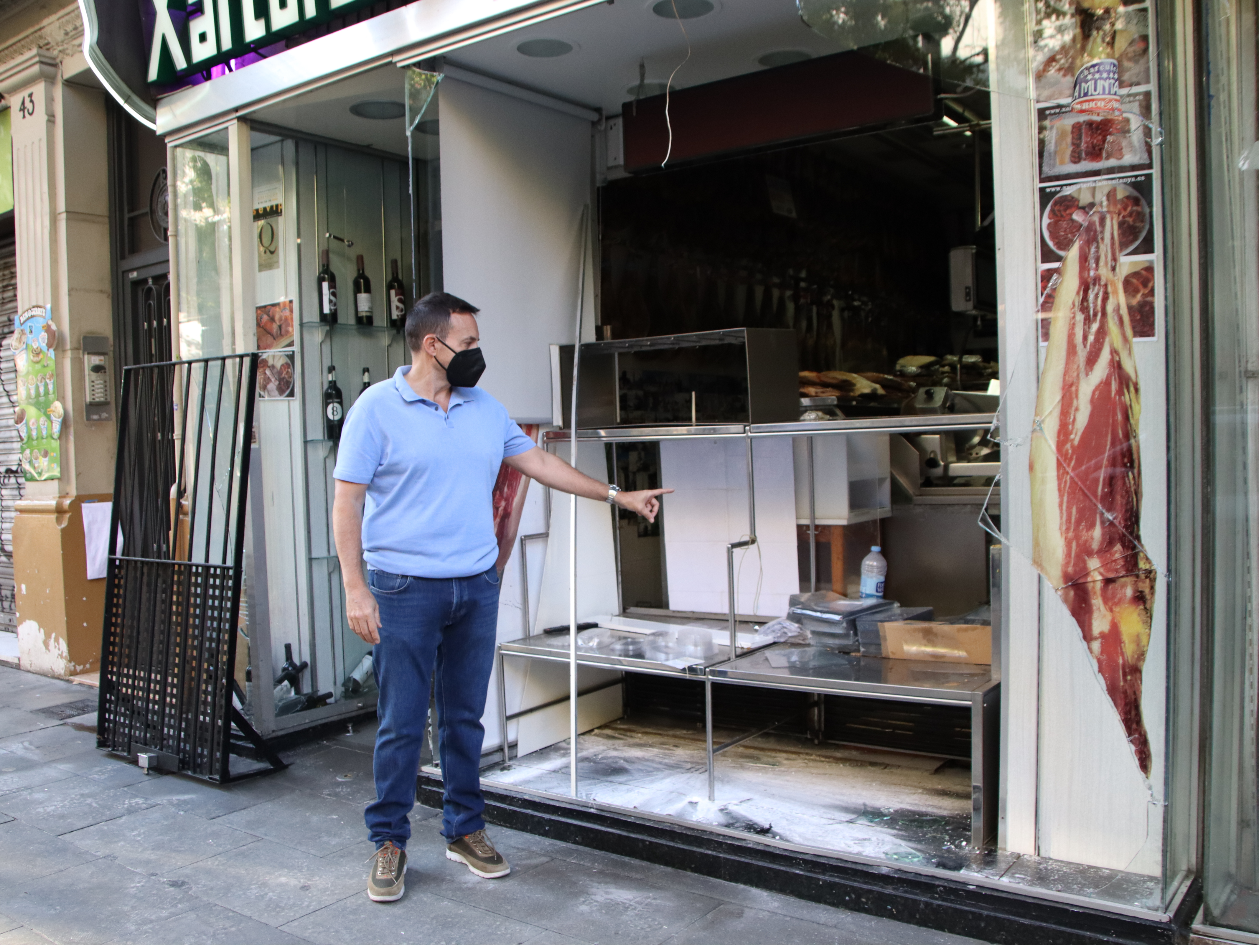 Sergio, the son of the La Muntanya charcuterie owner on Barcelona's Creu Coberta street, points at windows destroyed by La Mercè looters