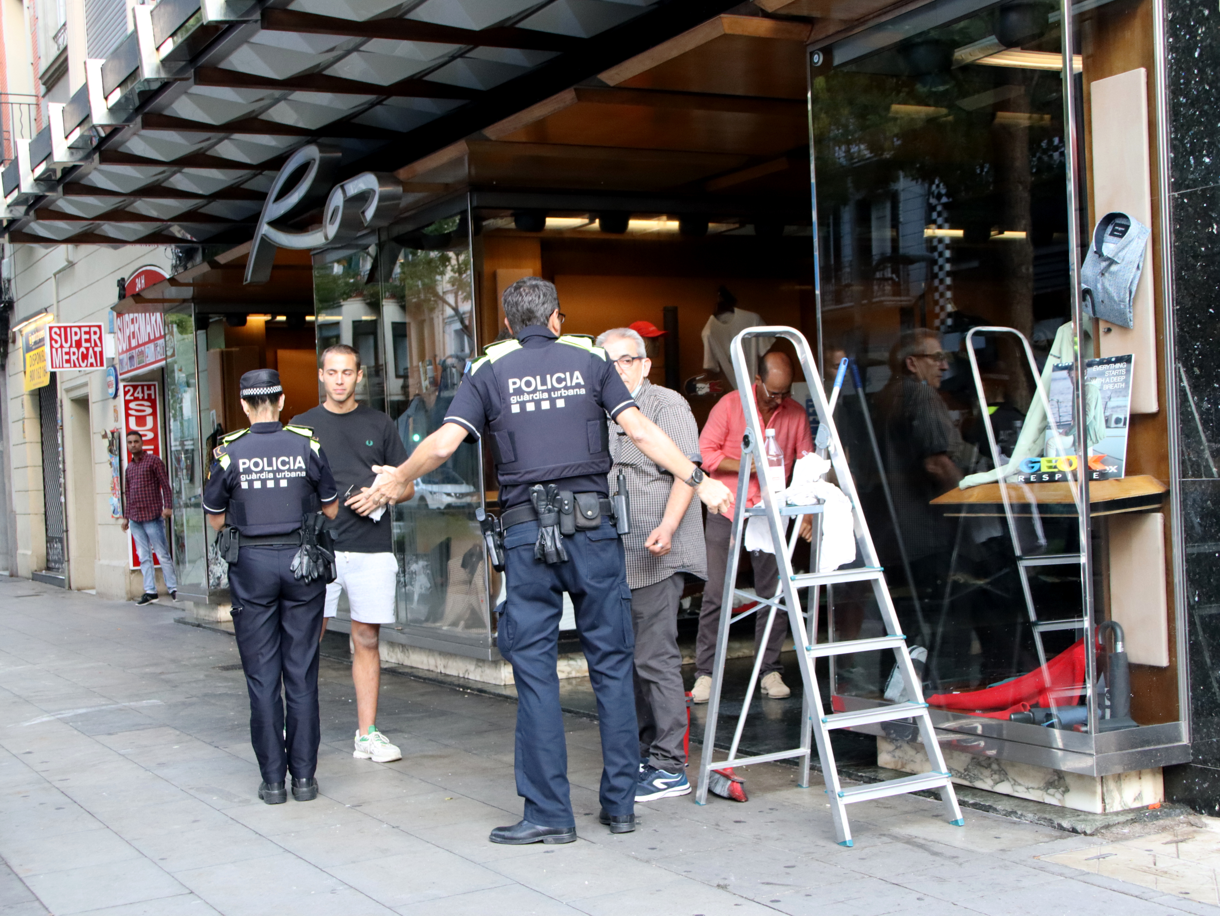 Police officers talking to a shopkeeper whose store was vandalized on Carrer Creu Coberta street in Barcelona on September 25, 2022
