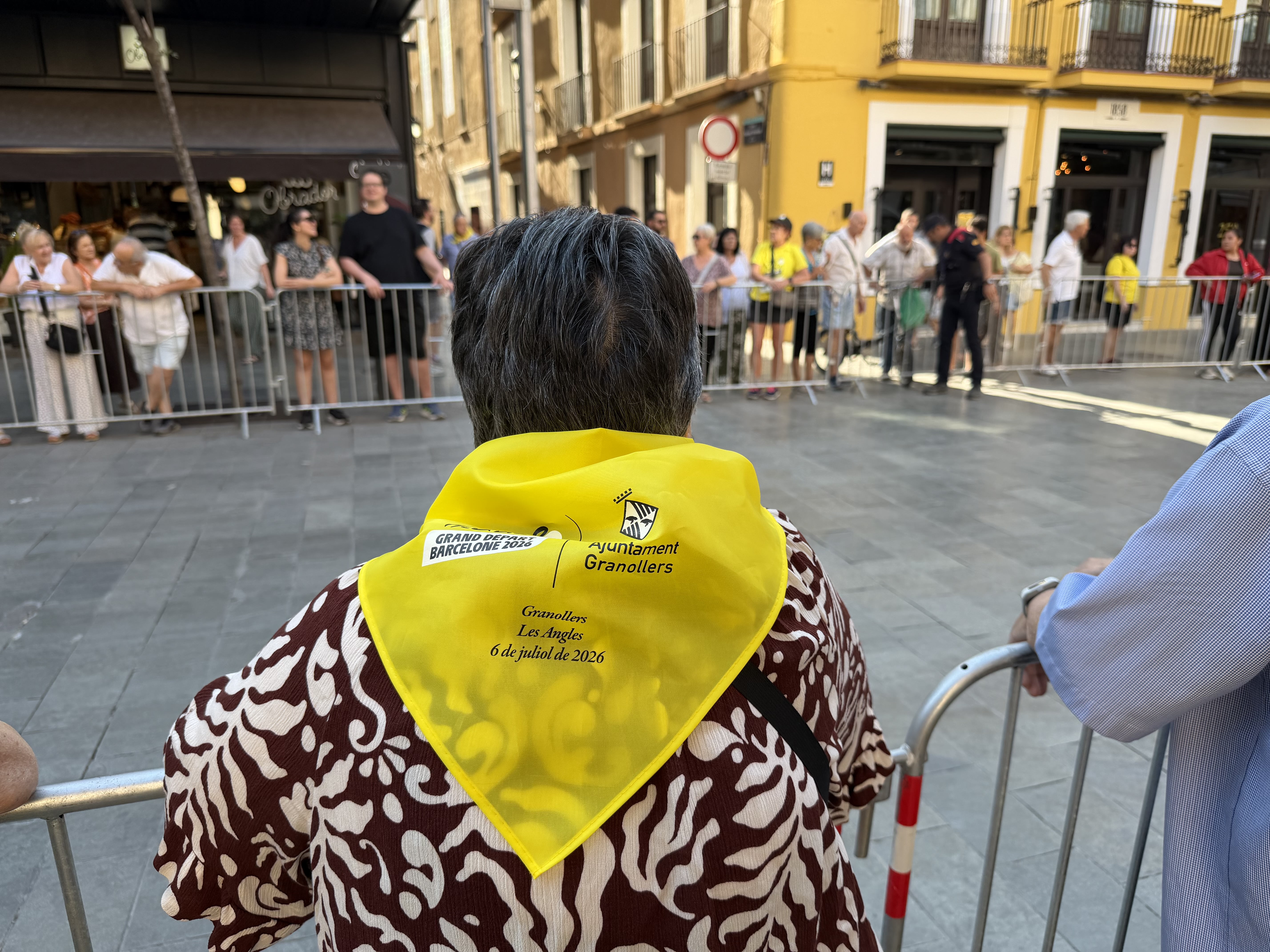 A woman with the scarf distributed by the City Council while waiting for cyclists to pass