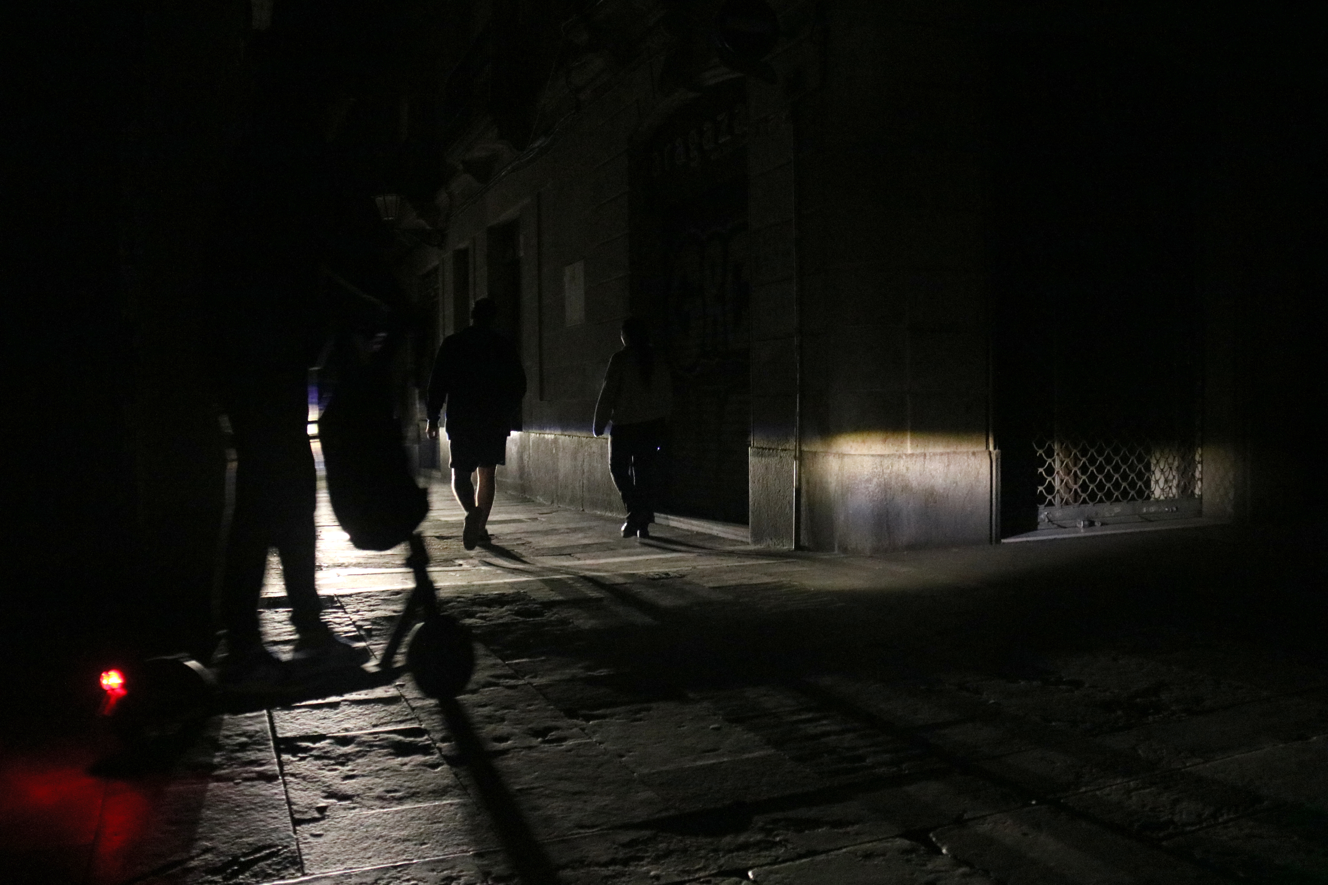 Un carrer del Barri Gòtic de Barcelona totalment fosc, amb la il·luminació d'un vehicle com a única llum