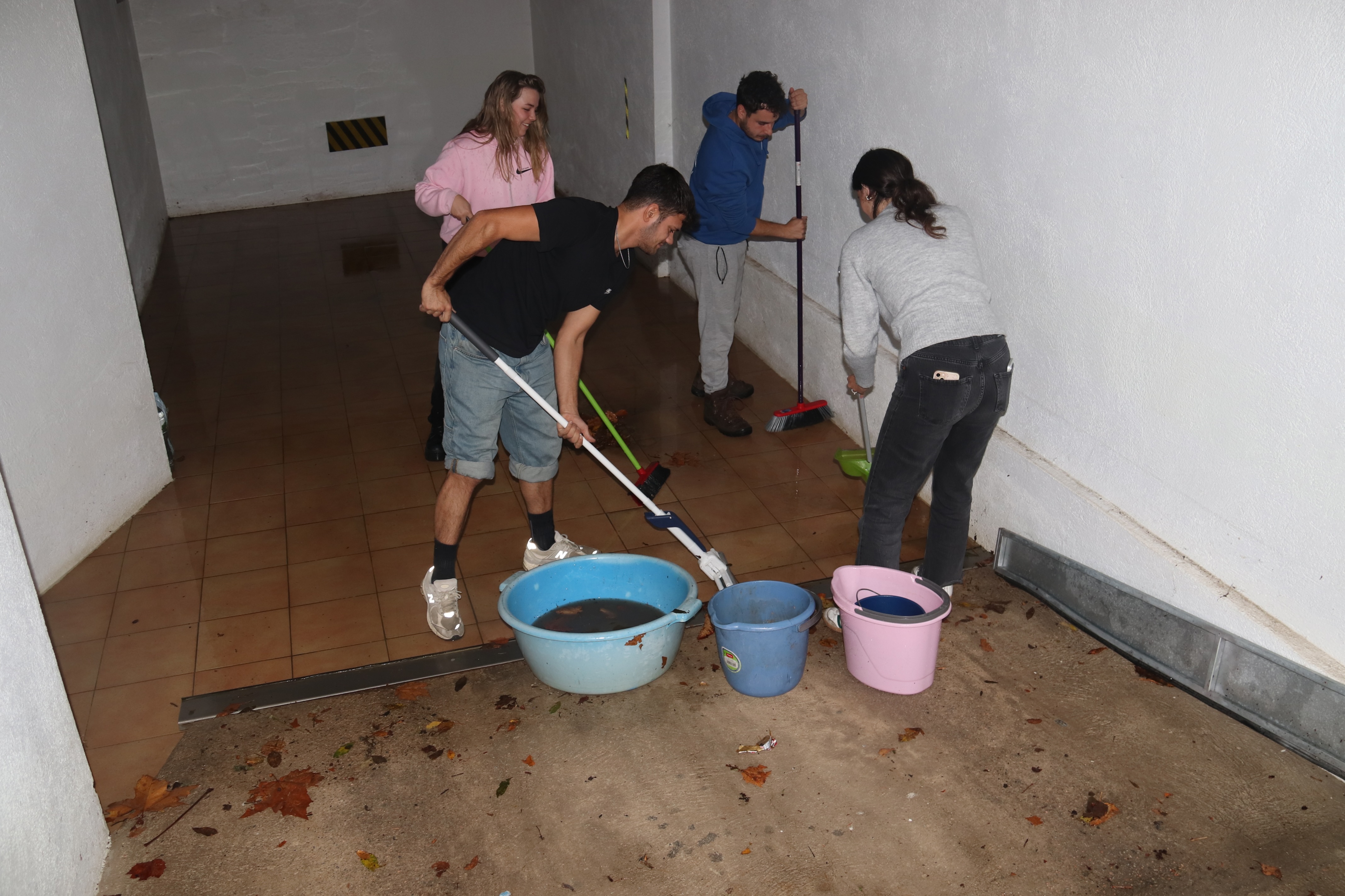 Un grup de joves treu aigua d’un pàrquing soterrat després dels aiguats