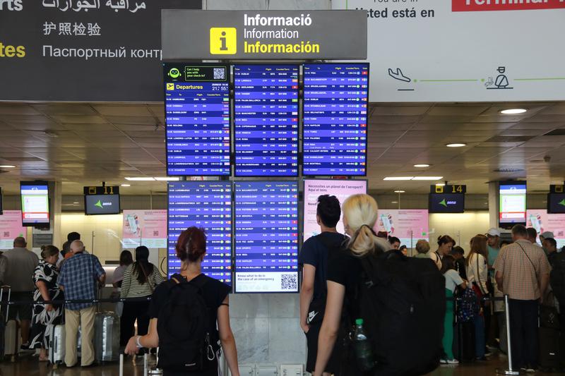 Passengers checking flight information screens at Terminal 2 of Barcelona airport