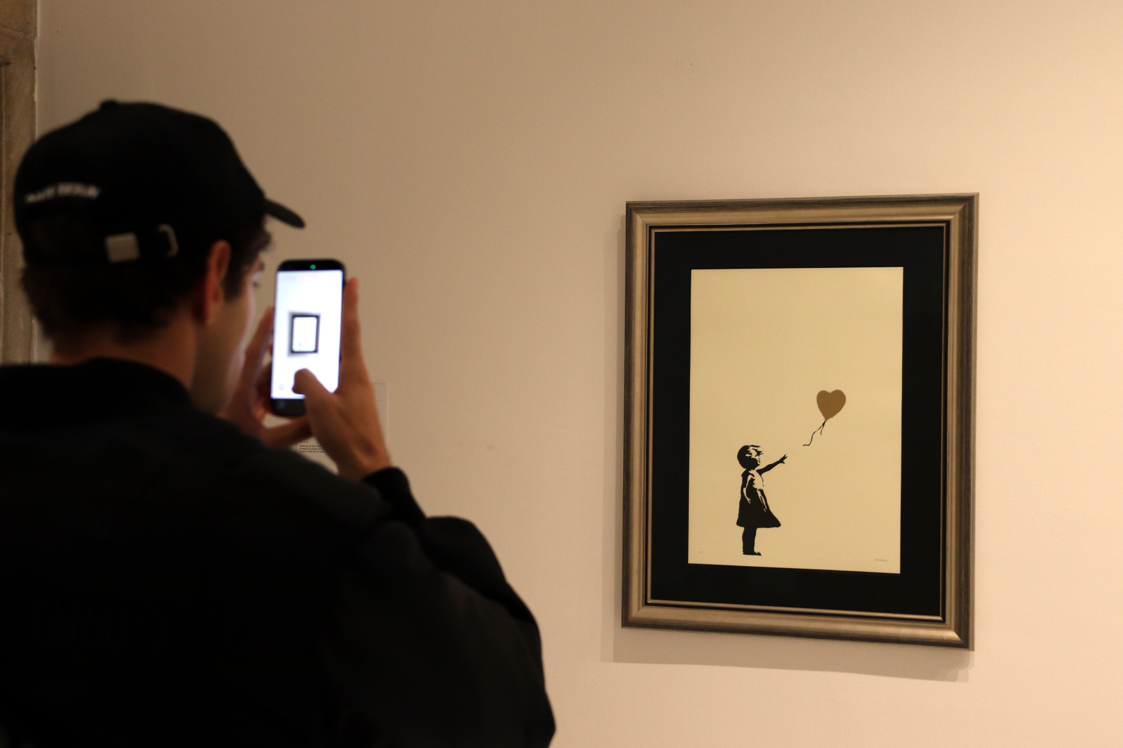 A person photographs an artwork of 'New works by Banksy,' featuring 25 authenticated works by the British artist at the Moco Museum Barcelona