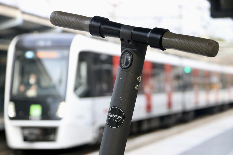 An electric scooter with an FGC train in the background