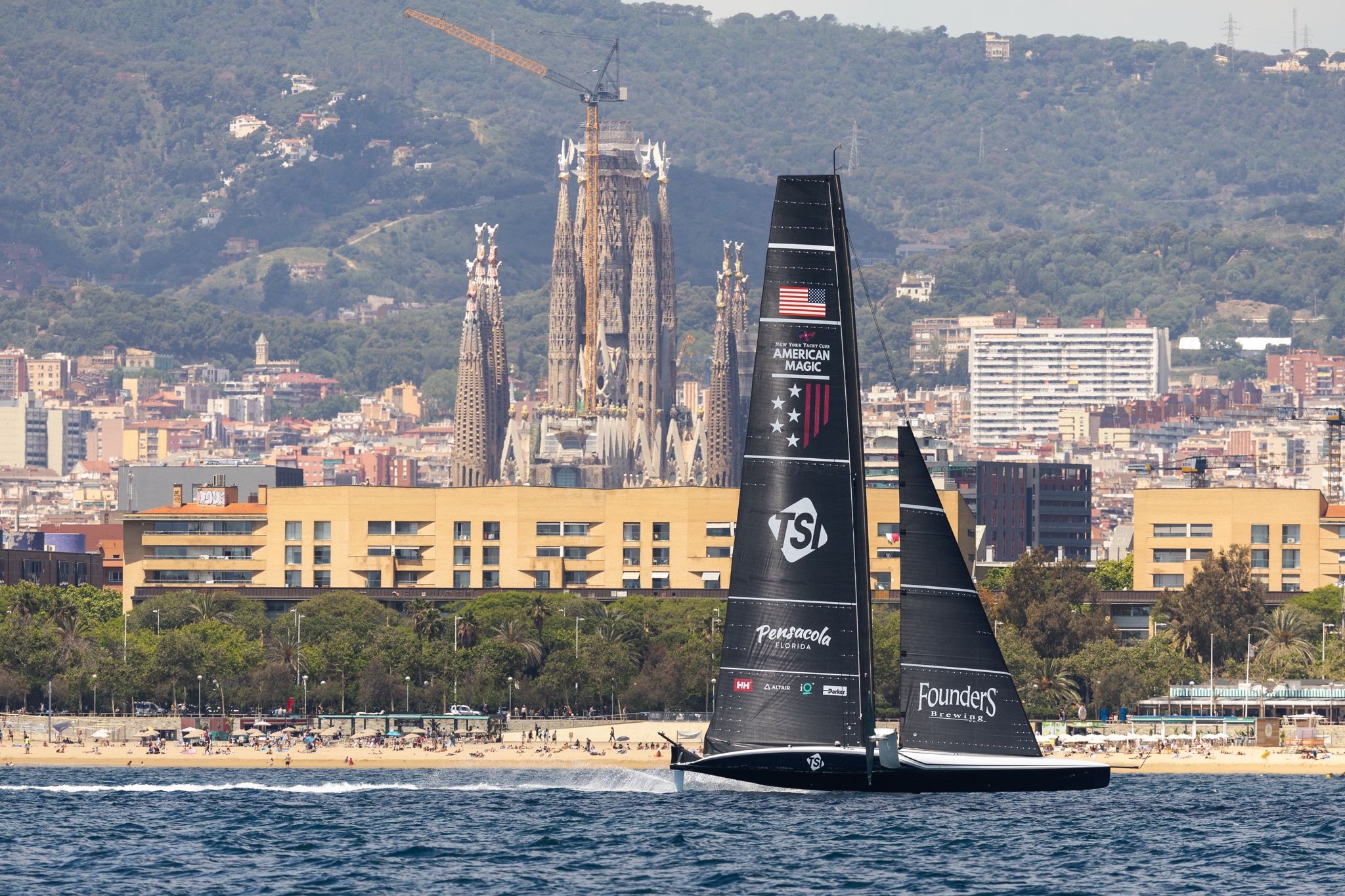 The American Magic boat, Patriot, sails in front of Barcelona's skyline with Sagrada Família in the background