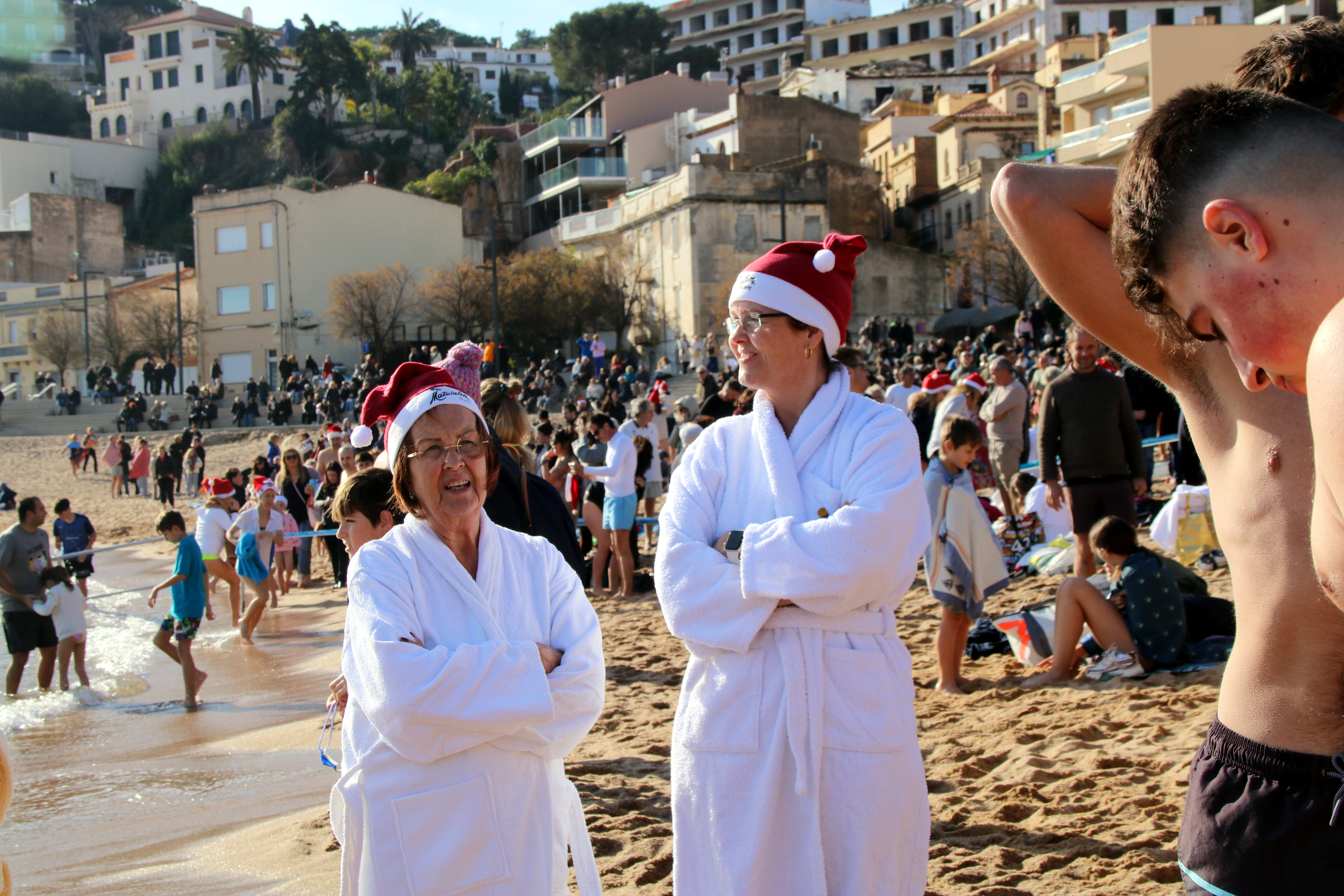 Dues dones, vestides amb albornos i gorros de Pare Noel, abans del primer bany de l'any a Sant Feliu de Guíxols