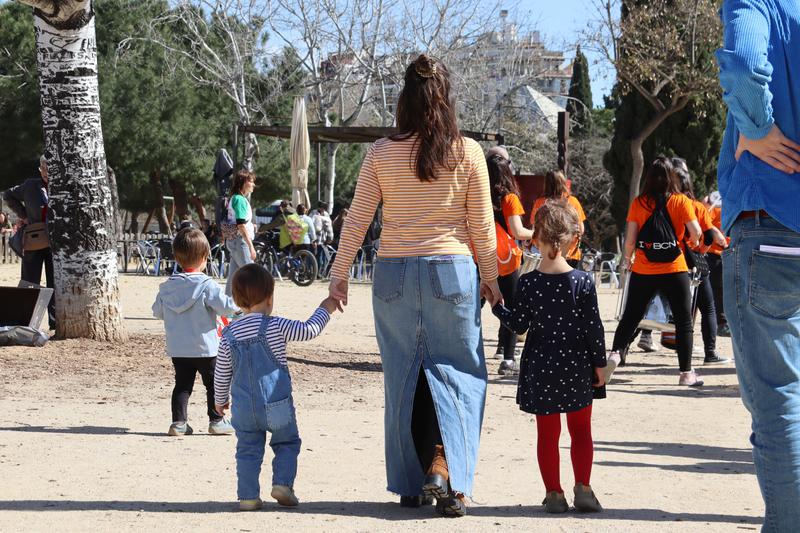 A mother holds her children's hands in a park in Barcelona