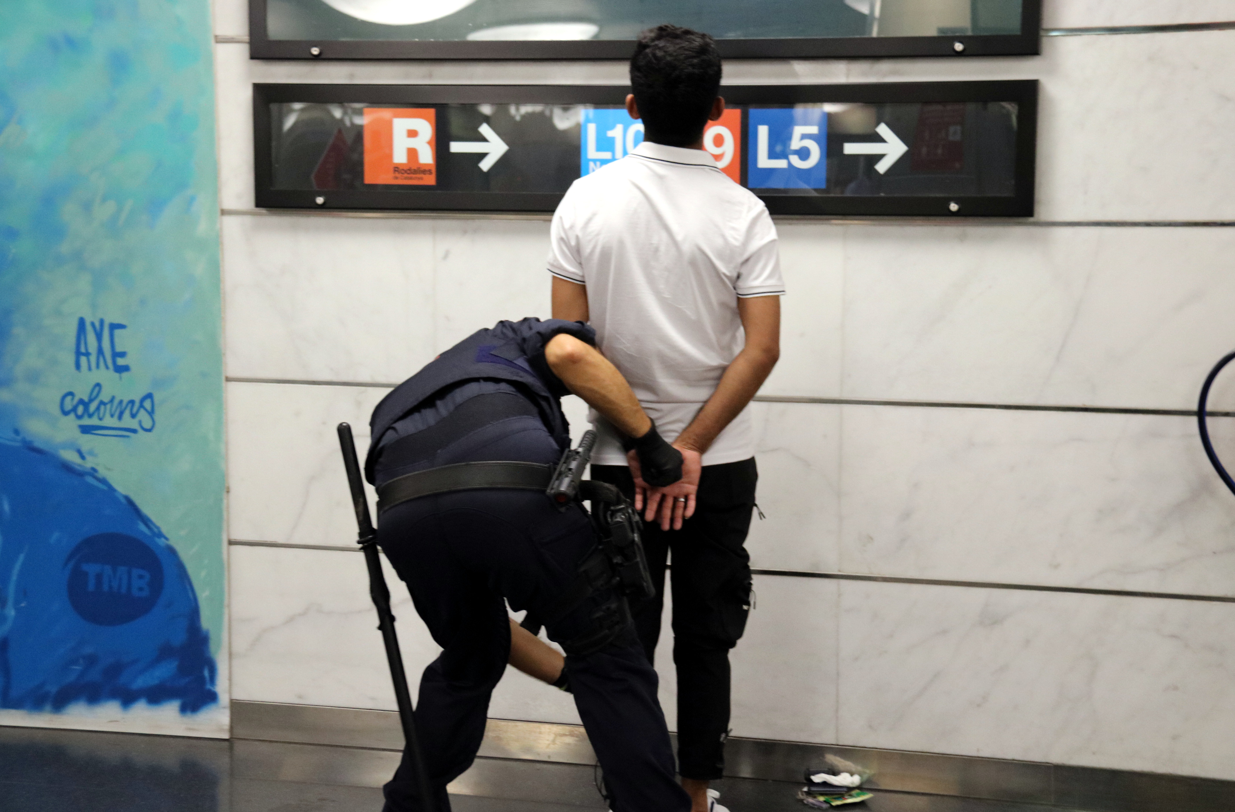 A Mossos d'Esquadra officer searching a man at La Sagrera station