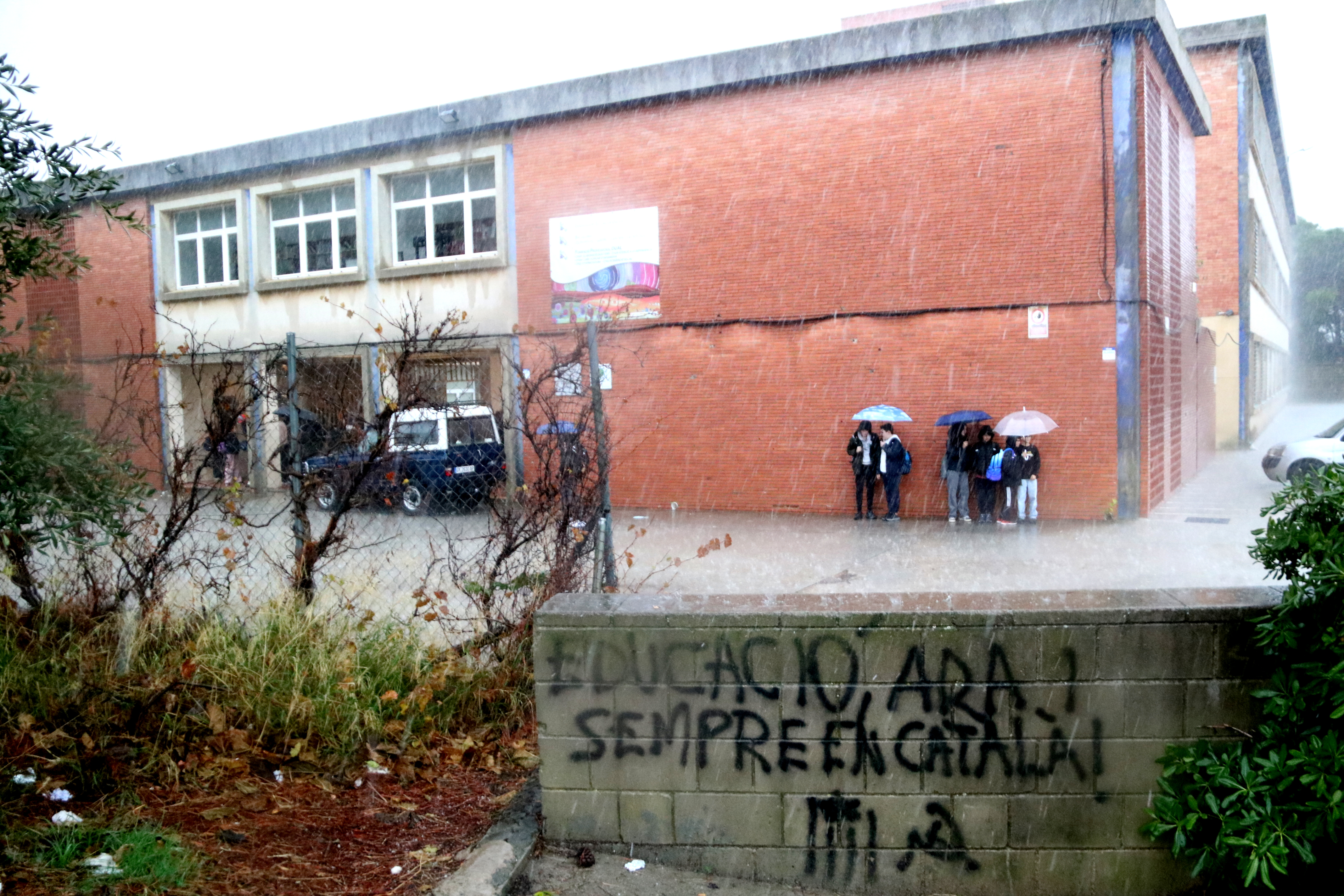 Students at the Institut Priorat in Falset wait under heavy rain