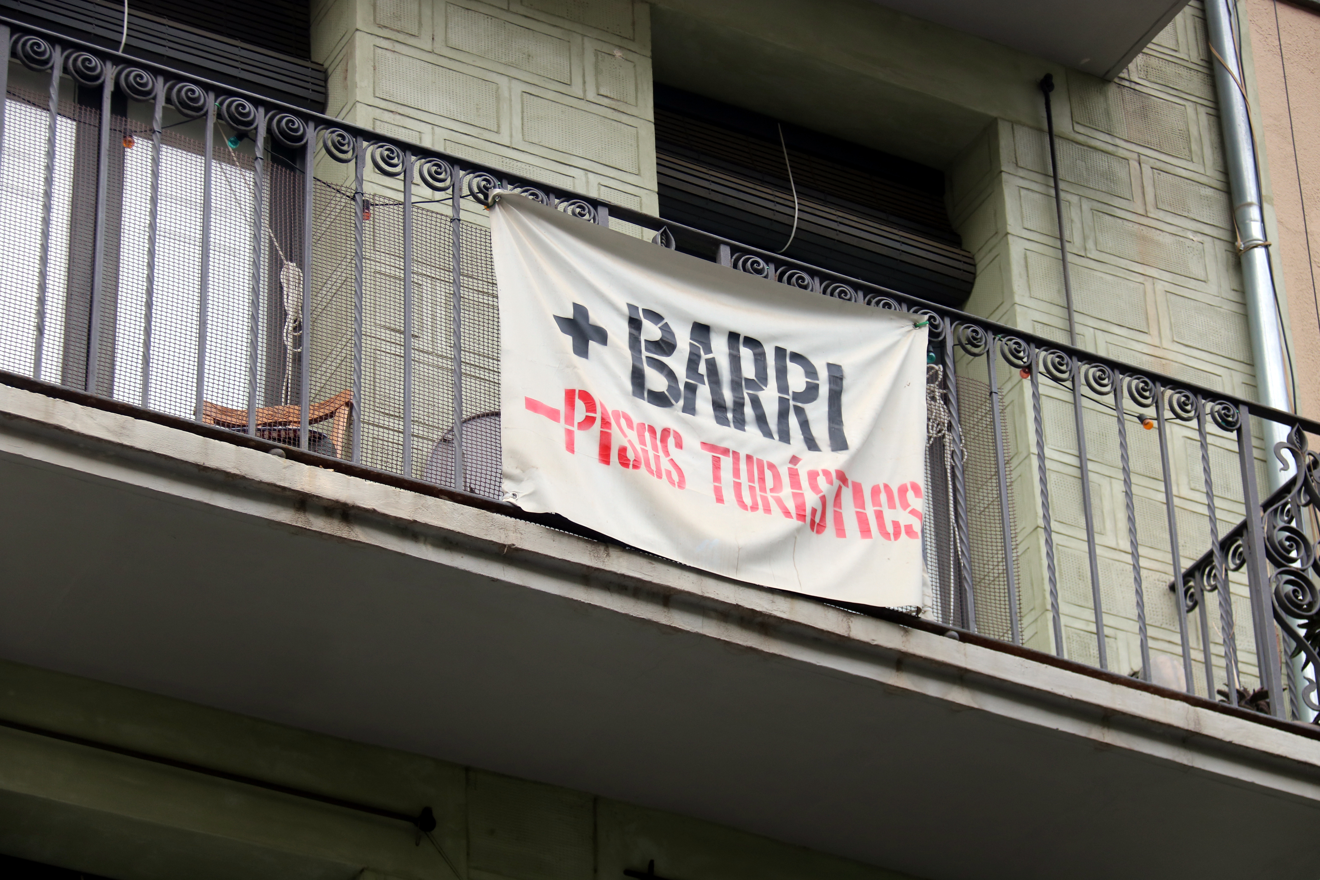 Sign with the slogan "+Neighborhood -Tourist Apartments" on a balcony in Girona.