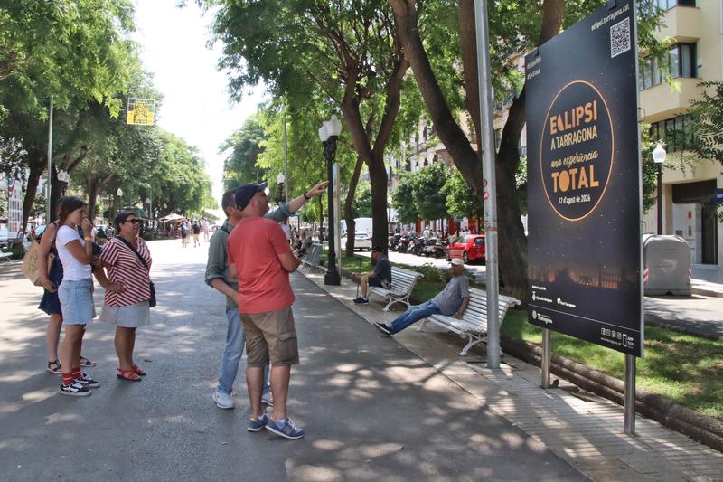 People looking at a poster announcing the total solar eclipse on La Rambla Nova in Tarragona