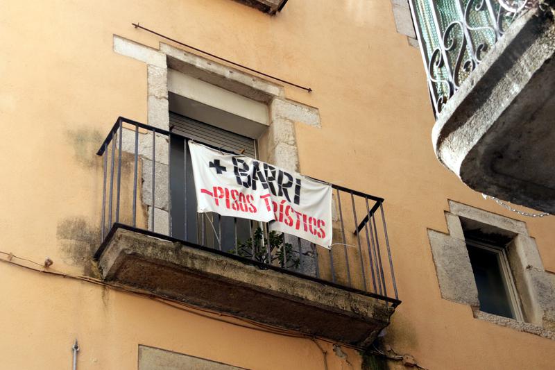 A poster reads: 'More neighborhood, fewer tourist apartments' from a balcony on Girona's Rambla boulevard