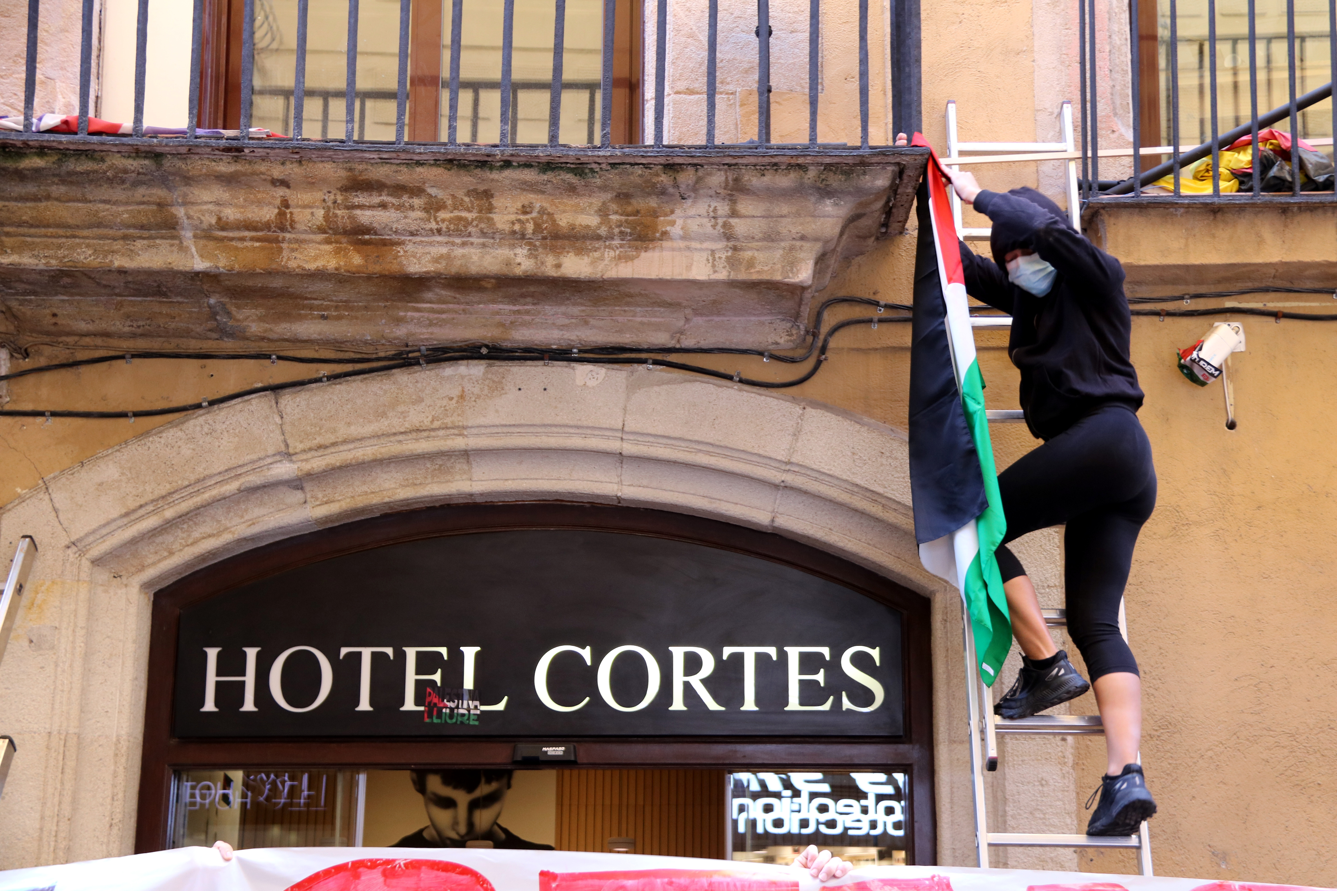 A Pro-Palestine protester hangs Palestinian flags on the façade of Barcelona's Cortés Hotel, owned by an Israeli tycoon, on October 21, 2023