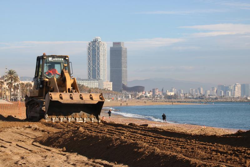 An excavator flattening sand on the San Sebastià beach in Barcelona