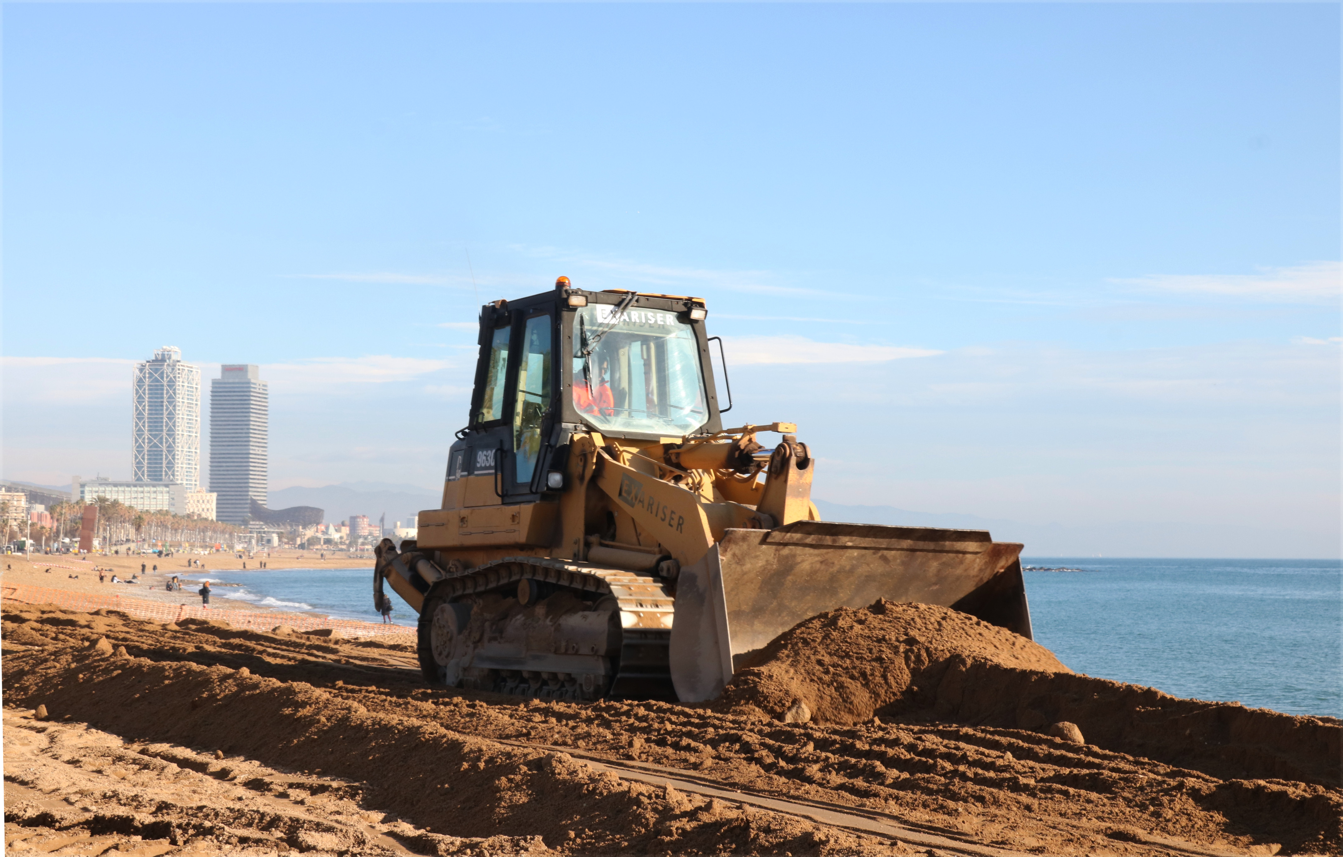 An excavator flattening sand on the San Sebastià beach in Barcelona on a weekday in January