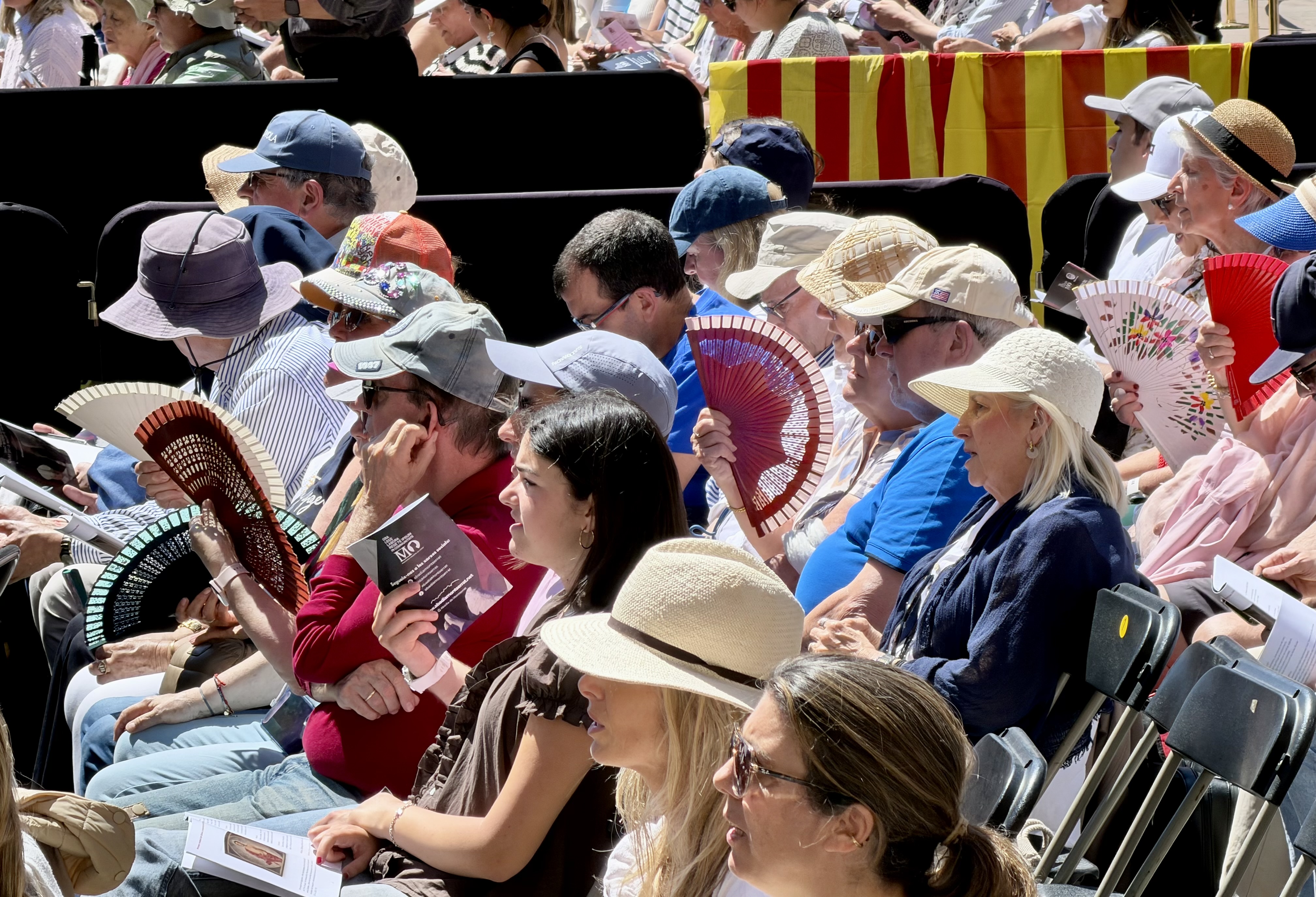 People shelter from the sun with hats and fans in the square outside Montserrat basilica