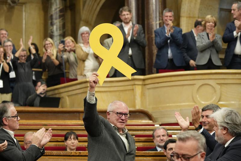 Former Minister of Culture and Junts MP Lluís Puig displays the yellow ribbon that occupied his empty seat in Parliament