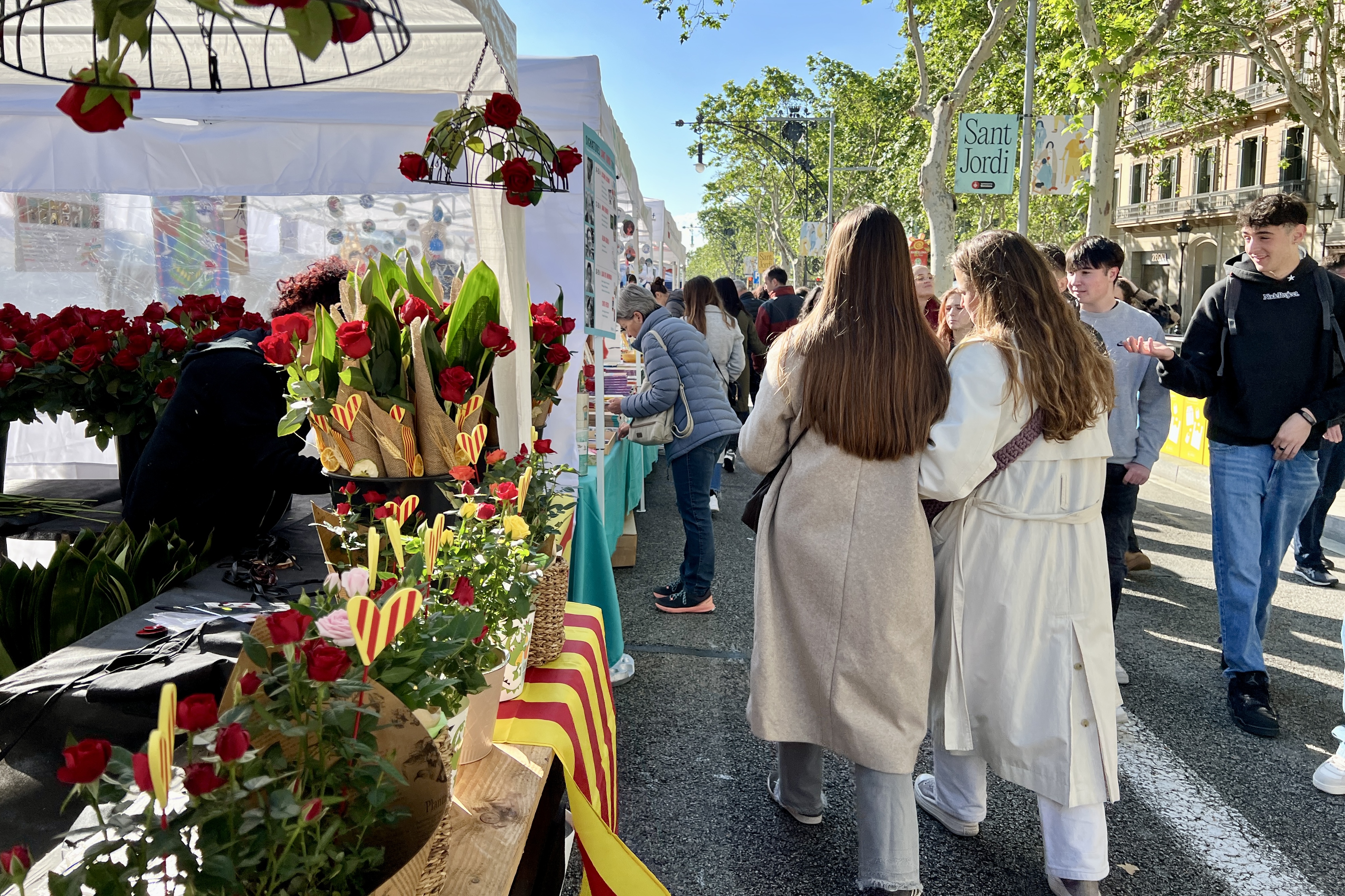 People walk in front of a rose stall on Passeig de Gràcia on Sant Jordi 2024