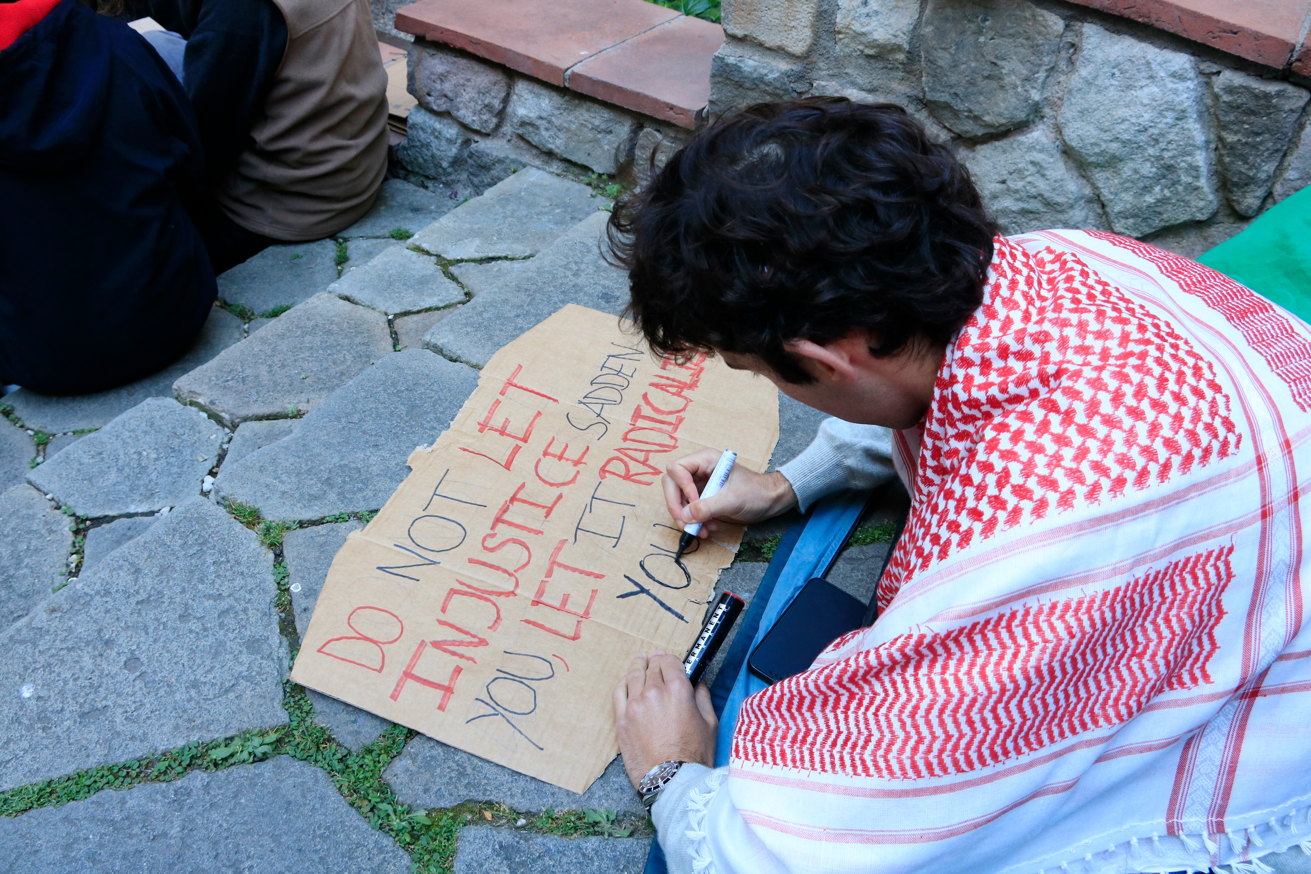 A student wearing a Palestinian keffiyeh scarf writing a poster after spending the night at the University of Barcelona cloister on May 7, 2024