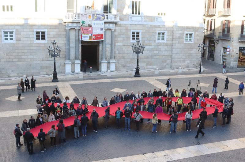Representatives of the December 1st Committee and health officials, including Minister Olga Pané, display a red ribbon at Barcelona's Plaça de Sant Jaume for World AIDS Day