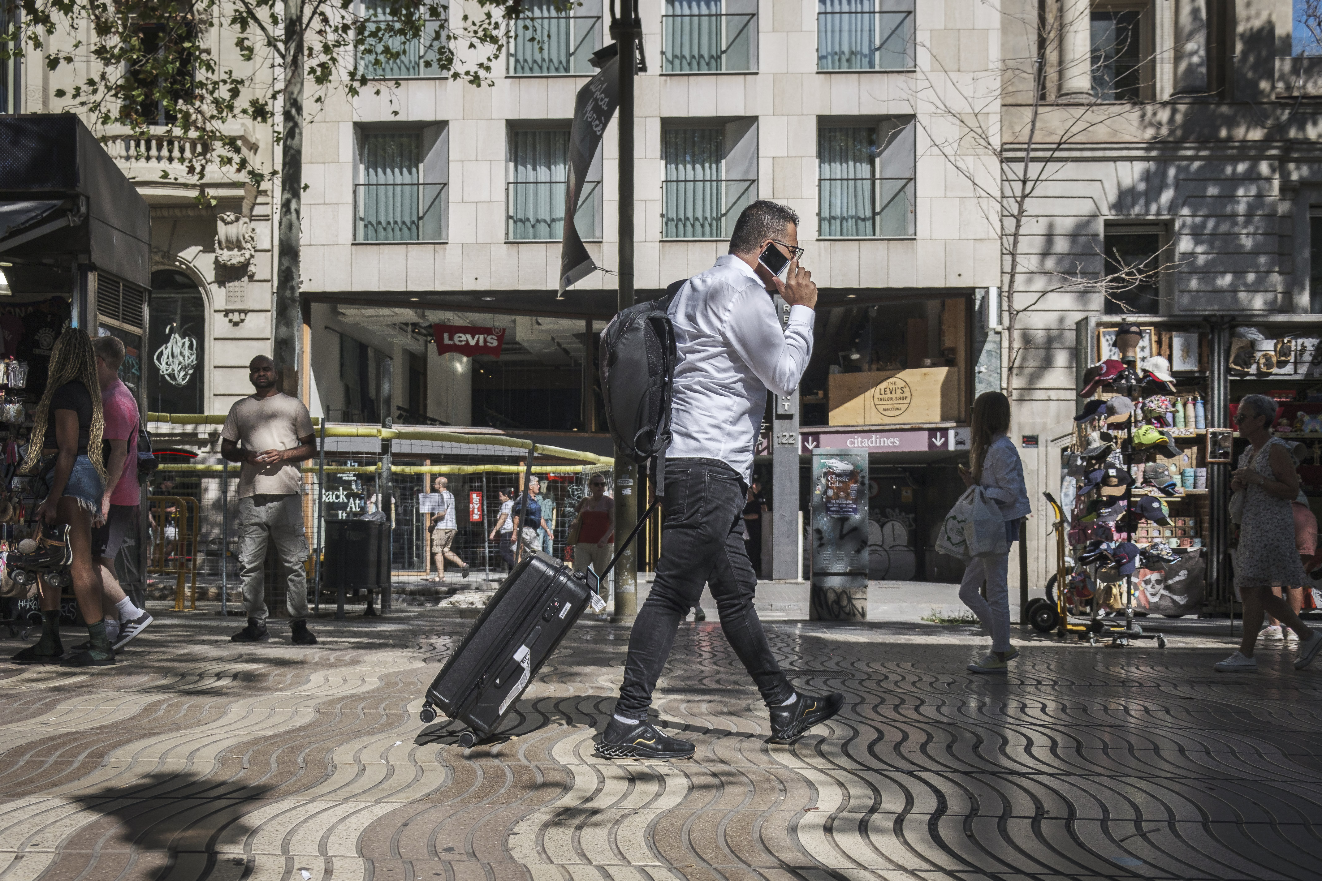 A tourist walks down La Rambla boulevard in Barcelona speaking on the phone and carrying a suitcase