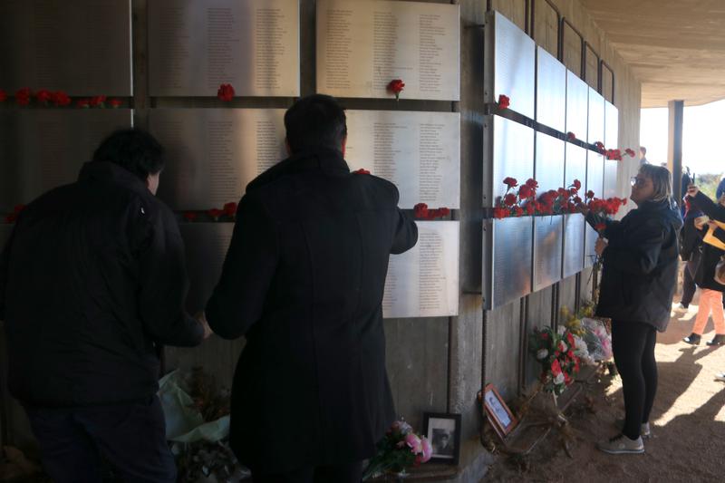 Several people place carnations at the Memorial 'Les Camposines" in La Fatarella