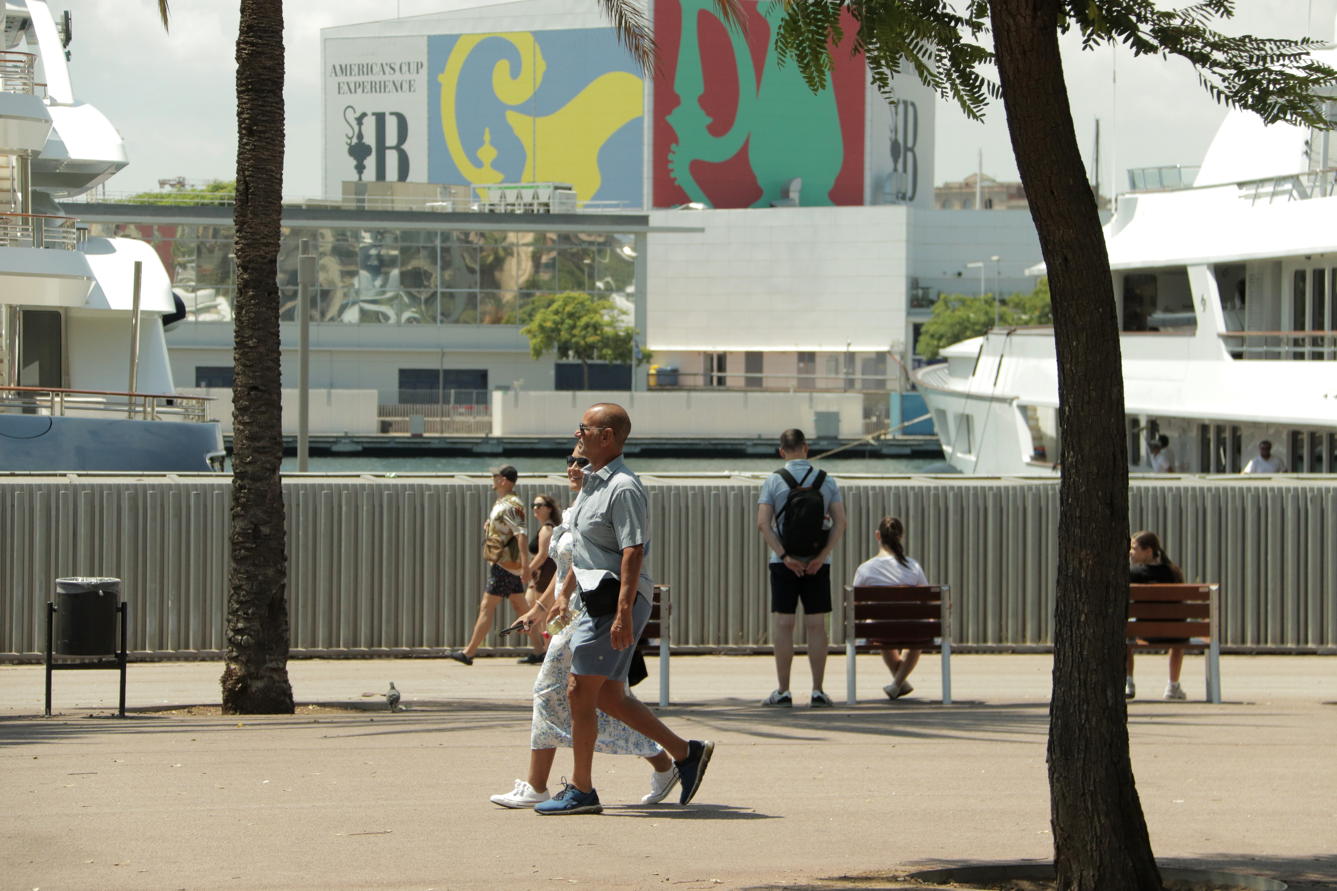 People walking through the neighbourhood of La Barceloneta with the branding of the America's Cup in the background