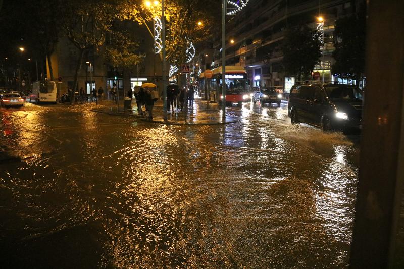 Several vehicles, including a bus, navigating the flooded Alfons XIII Street in Badalona near the Sant Roc neighborhood during heavy rain