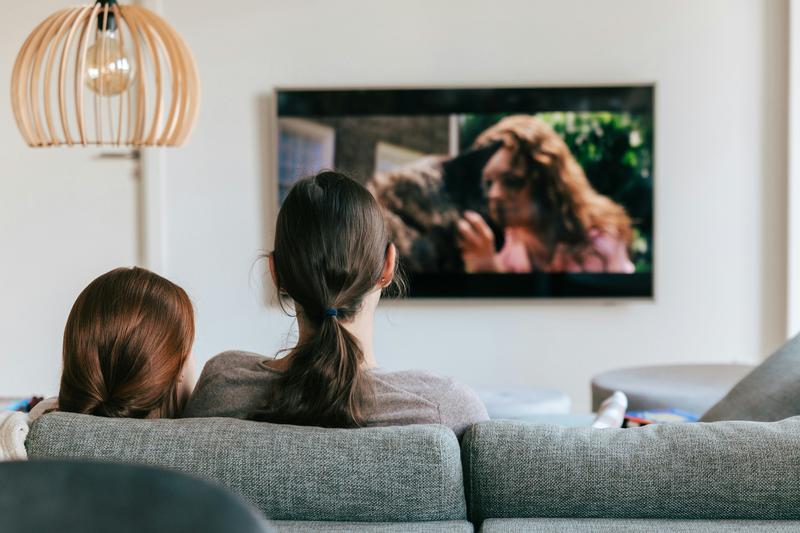 A couple of women sitting on a sofa watching television