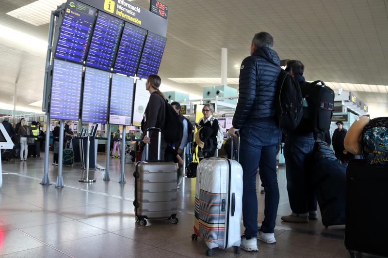 Passengers at Barcelona Airport observe the check-in screens in Terminal 1