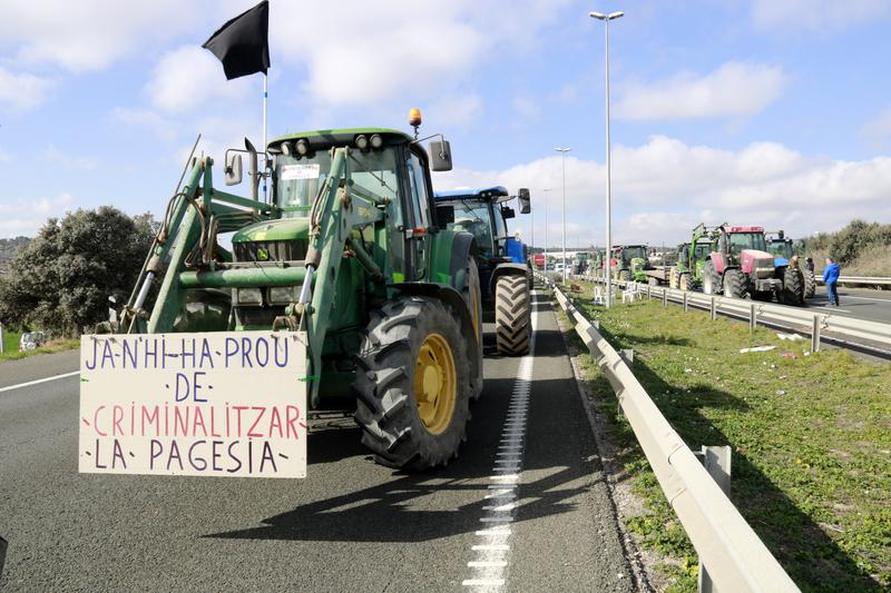 A tractor with a sign reading 'Enough criminalizing of farming' at the A-2 in Tàrrega