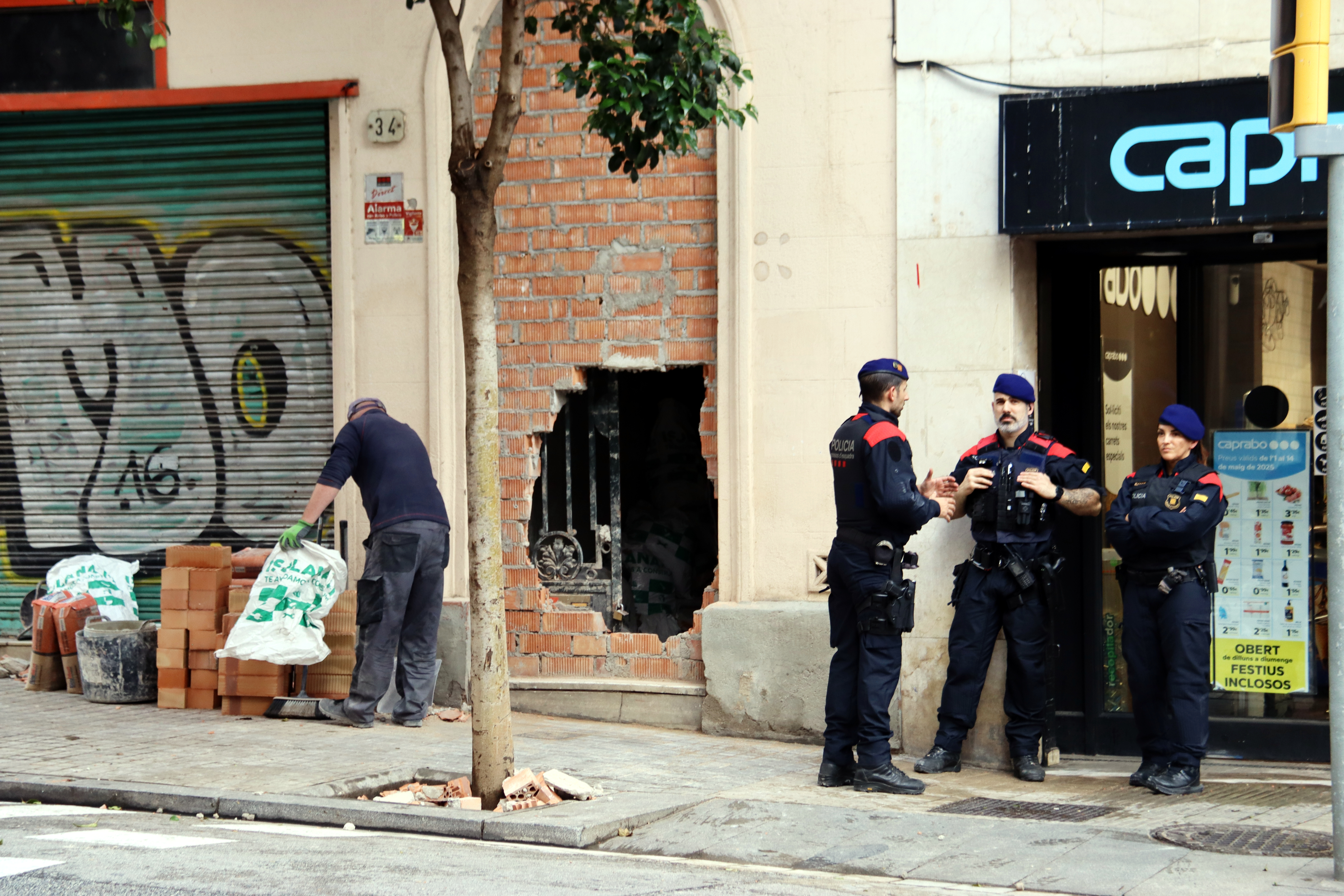Mossos d'Esquadra davant l'edifici ocupat a Vallcarca mentre un operari reconstrueix la tàpia.
